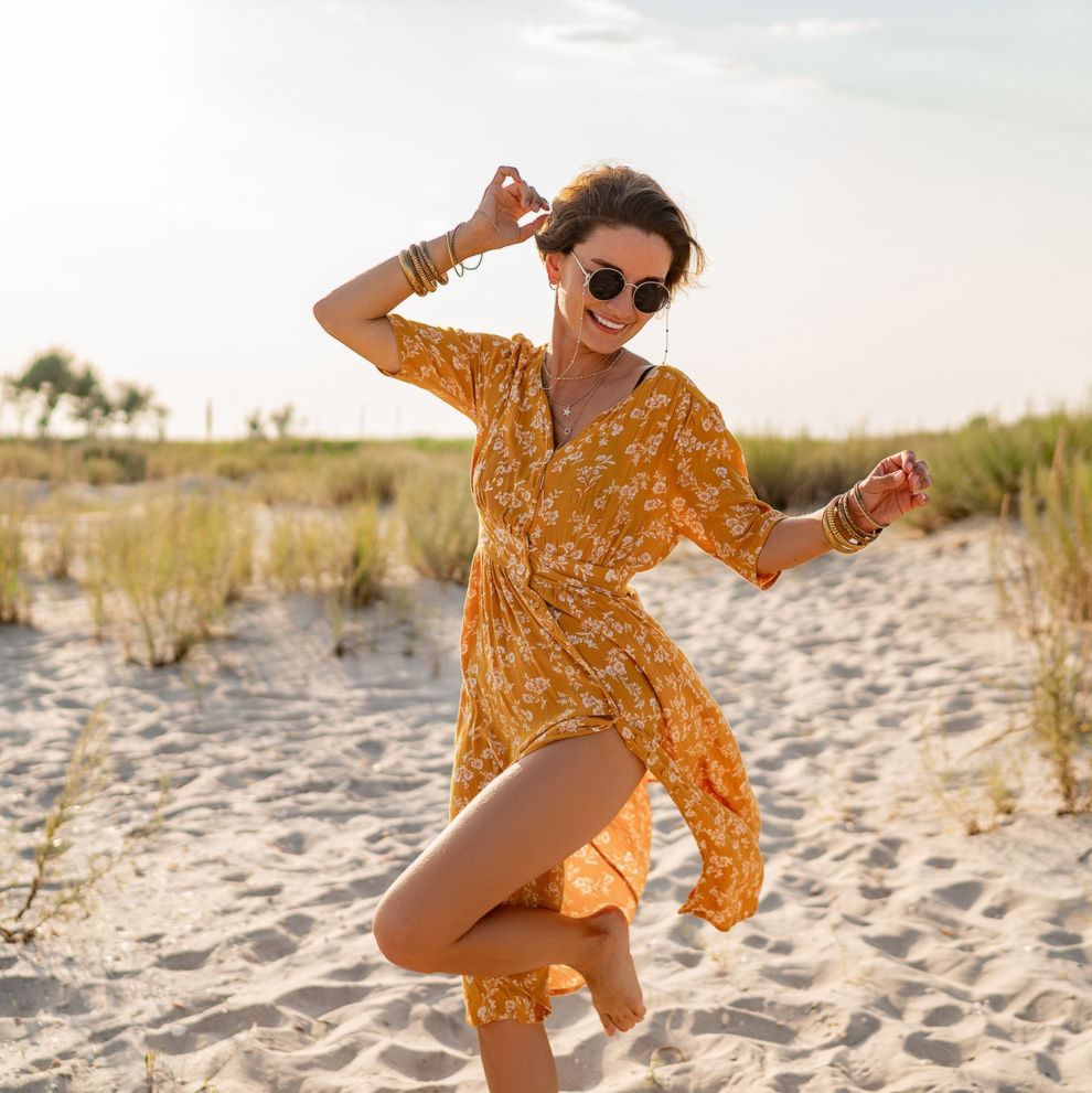 Photo of a young woman in a summer dress dancing on the beach