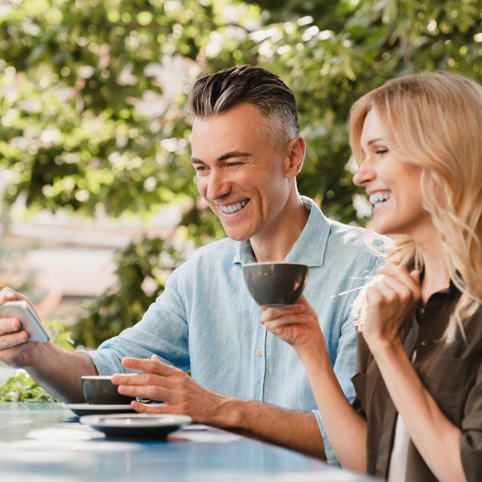 Photo of a middle-aged couple with healthy skin drinking coffee and looking at a smartphone