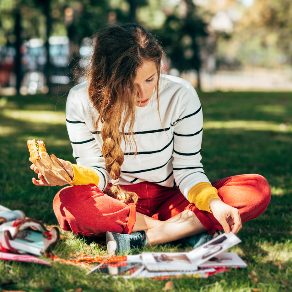 Photo of a young woman reading while enjoying a picnic in the park